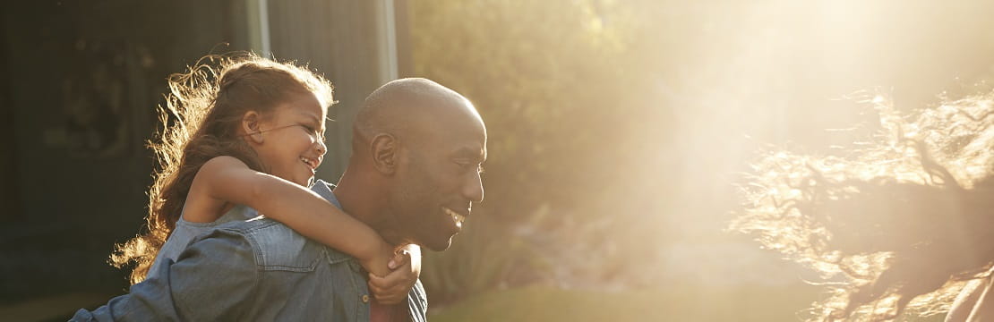 Man plays with his family in a backyard with his daughter on his back. 